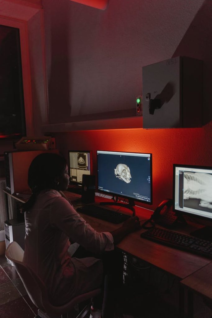 An osteologist studies skeletal images on computer monitors in a dimly lit lab.
