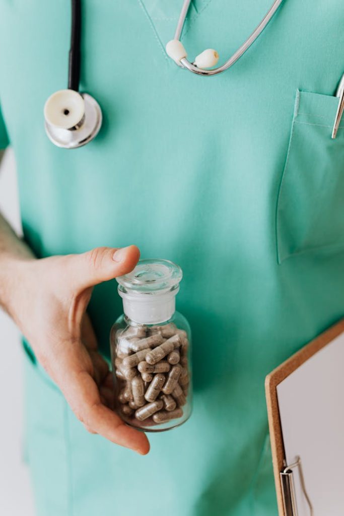 Anonymous crop man in light green medical uniform with stethoscope standing with clipboard and holding vial with drug in clinic